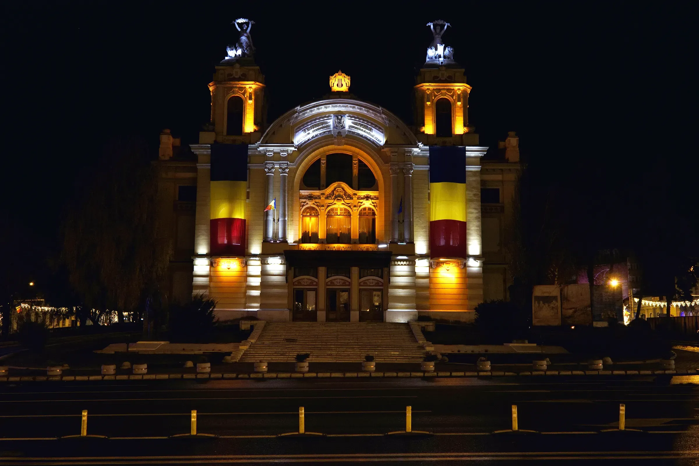 The front of the National Opera and National Theatre at night, with flags on the columns