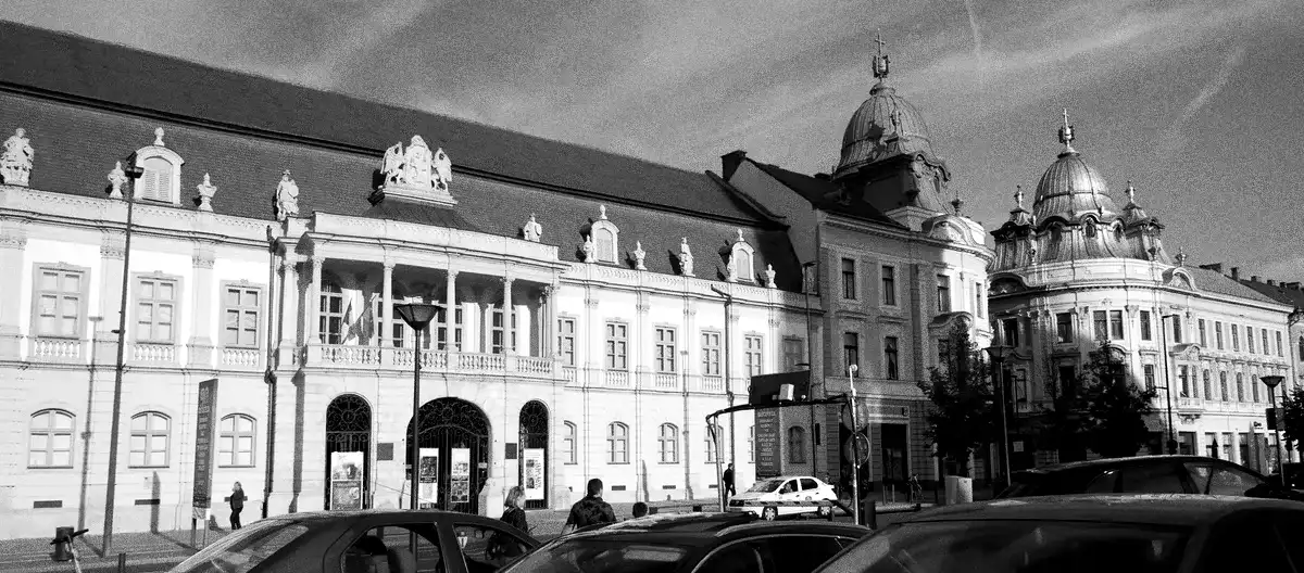 The Bánffy Palace at Piața Unirii 30, which houses the Art Museum. Above the portico, the Bánffy arms with their griffins; along the balustrade, the mythological statues. On the right, the twin Palaces of the Roman Catholic Status.