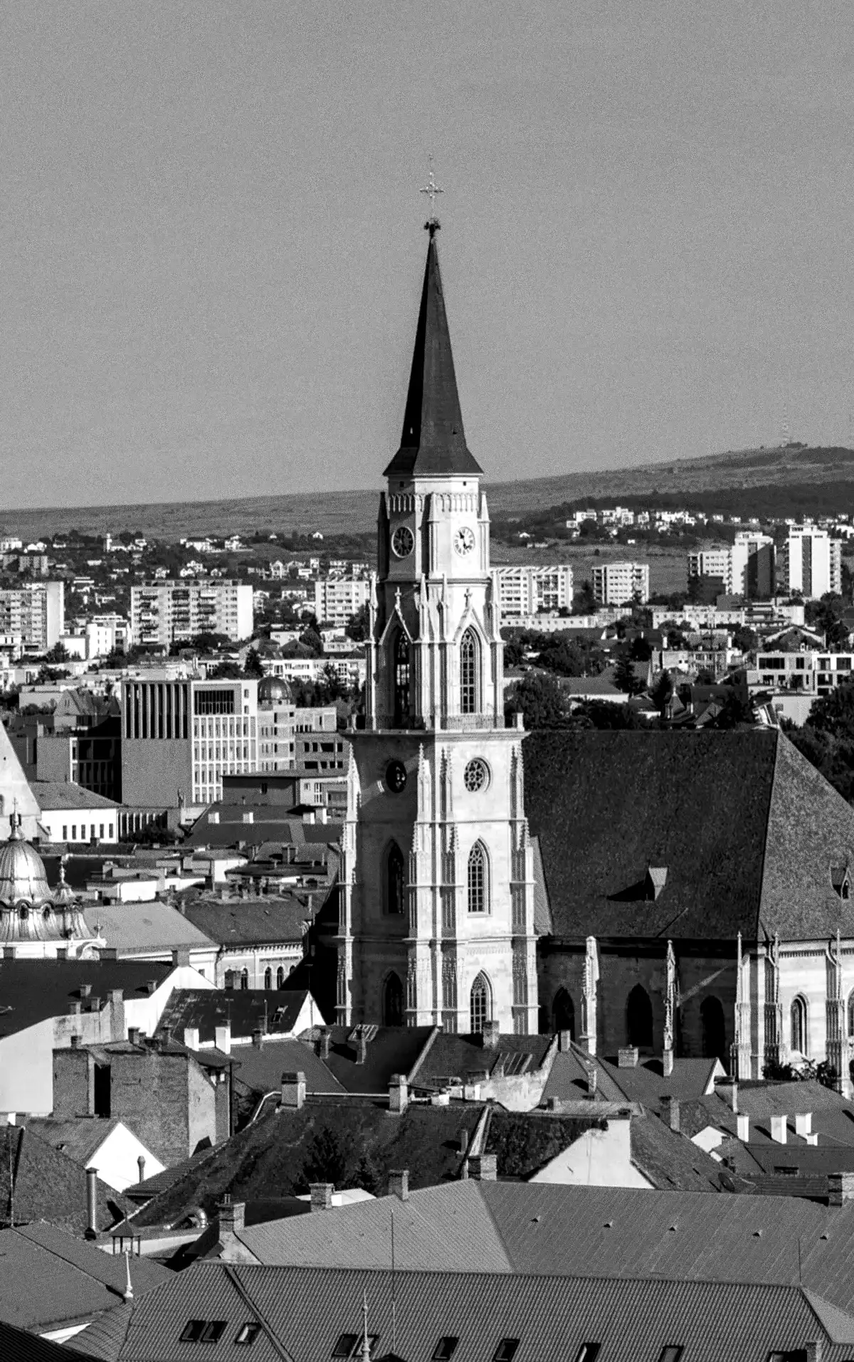 The tower of St Michael’s Church above the rooftops, hills behind, in black and white
